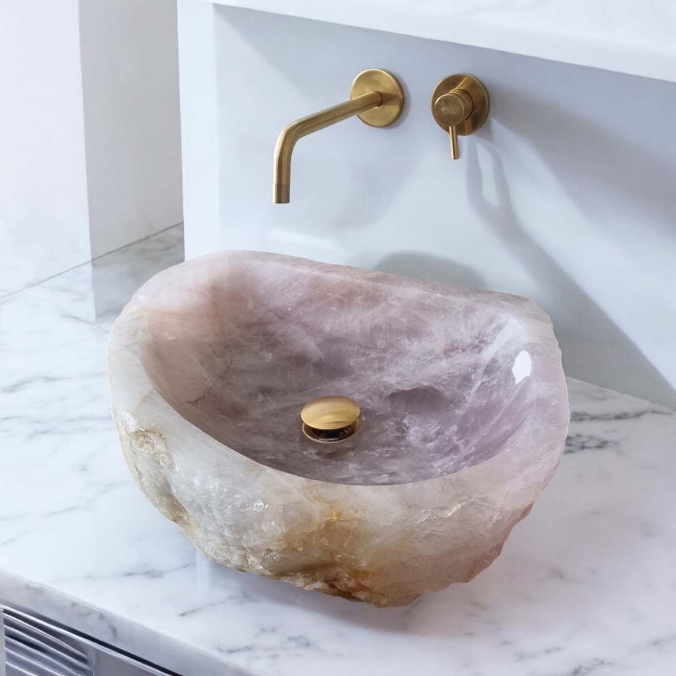 Rose quartz vessel sink on a white marble counter with brushed brass wall fixtures