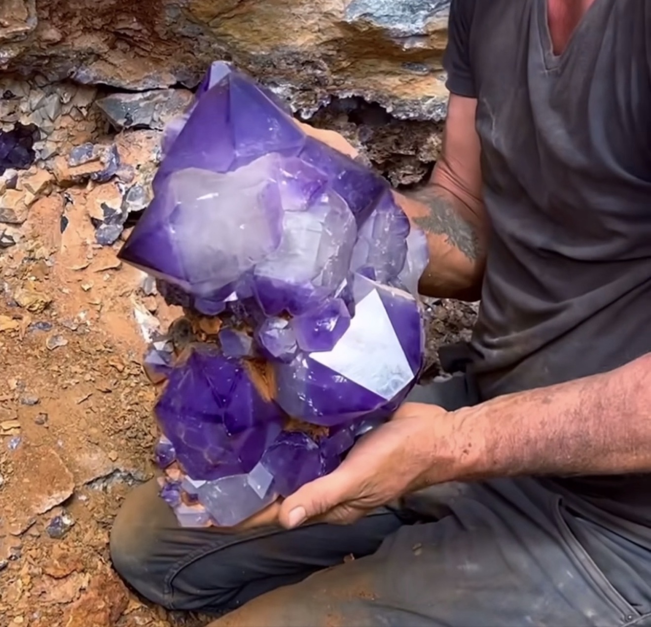 A miner at the rock face holding a huge violet amethyst cluster just extracted